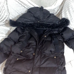 Svart pufferjacka med pälsdetaljer - Säljer en svart pufferjacka glorias gangster med pälsdetaljer på huvan. Jackan har dragkedja och knappar framtill samt flera praktiska fickor. Perfekt för kalla dagar.