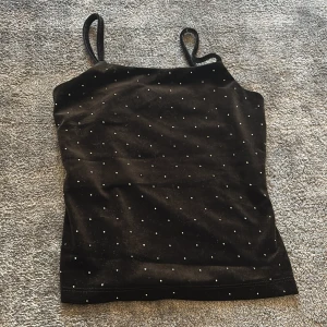 Svart glittrig tubtopp - Snygg svart tubtopp med glittriga detaljer. Perfekt för en kväll ute eller en festlig tillställning. Axelbandslös design som ger en stilren look.