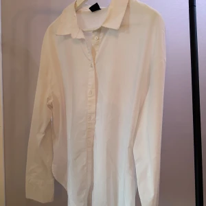 Vit långärmad skjorta, Gina Tricot  - Klassisk vit långärmad skjorta med knappar framtill. Perfekt för en stilren look. Skjortan har en enkel krage och är tillverkad i ett lätt material. Från Gina Tricot
