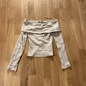 Beige offshoulder topp från Gina Tricot i storlek xs - Säljer en stilren beige offshoulder topp från Gina Tricot i ribbat material. Perfekt för en trendig look med långa ärmar och en elegant passform. Passar utmärkt till både vardag och fest.