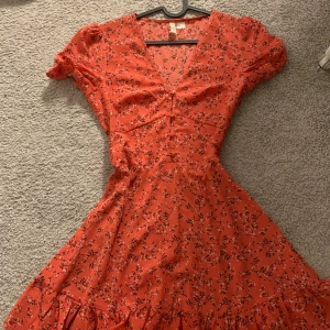 Röd blommig klänning från H&M - Charmig röd klänning med blommigt mönster från H&M. Den har en v-ringad design och korta ärmar, perfekt för en somrig look. 