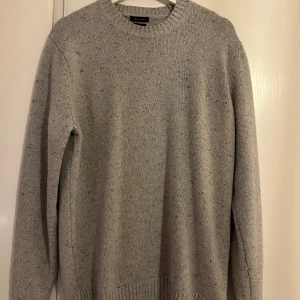 Grå stickad tröja från Massimo Dutti - Snygg grå stickad tröja från Massimo Dutti. Perfekt för kyliga dagar med sin mjuka och bekväma passform. Tröjan har en klassisk rund hals och ribbade kanter vid ärmslut och nederkant.