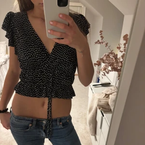 Svart och vit prickig topp - Säljer en snygg svart omlottopp med vita prickar. 