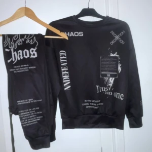 Svart sweatshirt och byxor med tryck - Säljer en svart sweatshirt och matchande byxor med tryck av text och grafiska element. Tröjan har långa ärmar och byxorna har elastisk midja. Perfekt för en avslappnad stil med en edgy touch.