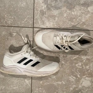 Vita paddelskor från Adidas - Säljer ett par vita paddelskor från Adidas med svarta ränder på sidan.