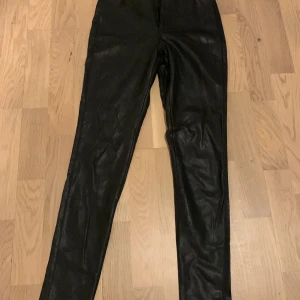 Svarta byxor i syntet från BikBok - Snygga svarta byxor i syntetmaterial från BikBok. De har en tight passform och hög midja, vilket ger en stilren look. Perfekta för att skapa en edgy outfit.