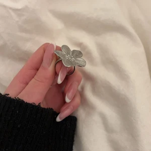 Silverfärgad blomring - Snygg och stilren ring i silverfärg med en stor blomma som detalj. Perfekt för att ge en extra touch till din outfit. Blomman har fina detaljer som ger ringen en unik look.