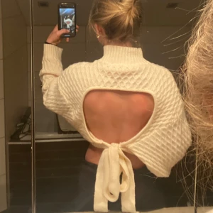 Vit stickad tröja med öppen rygg - Säljer en snygg vit stickad tröja med öppen rygg och knytning. Tröjan är croppad och har långa ärmar med ett fint mönster. Använd endast en gång! Superskönt💕💕