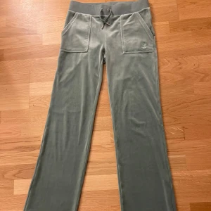 Grå mjukisbyxor från Juicy Couture - Snygga och bekväma grå mjukisbyxor från Juicy Couture med snörning i midjan och praktiska fickor framtill. Perfekta för en avslappnad stil.