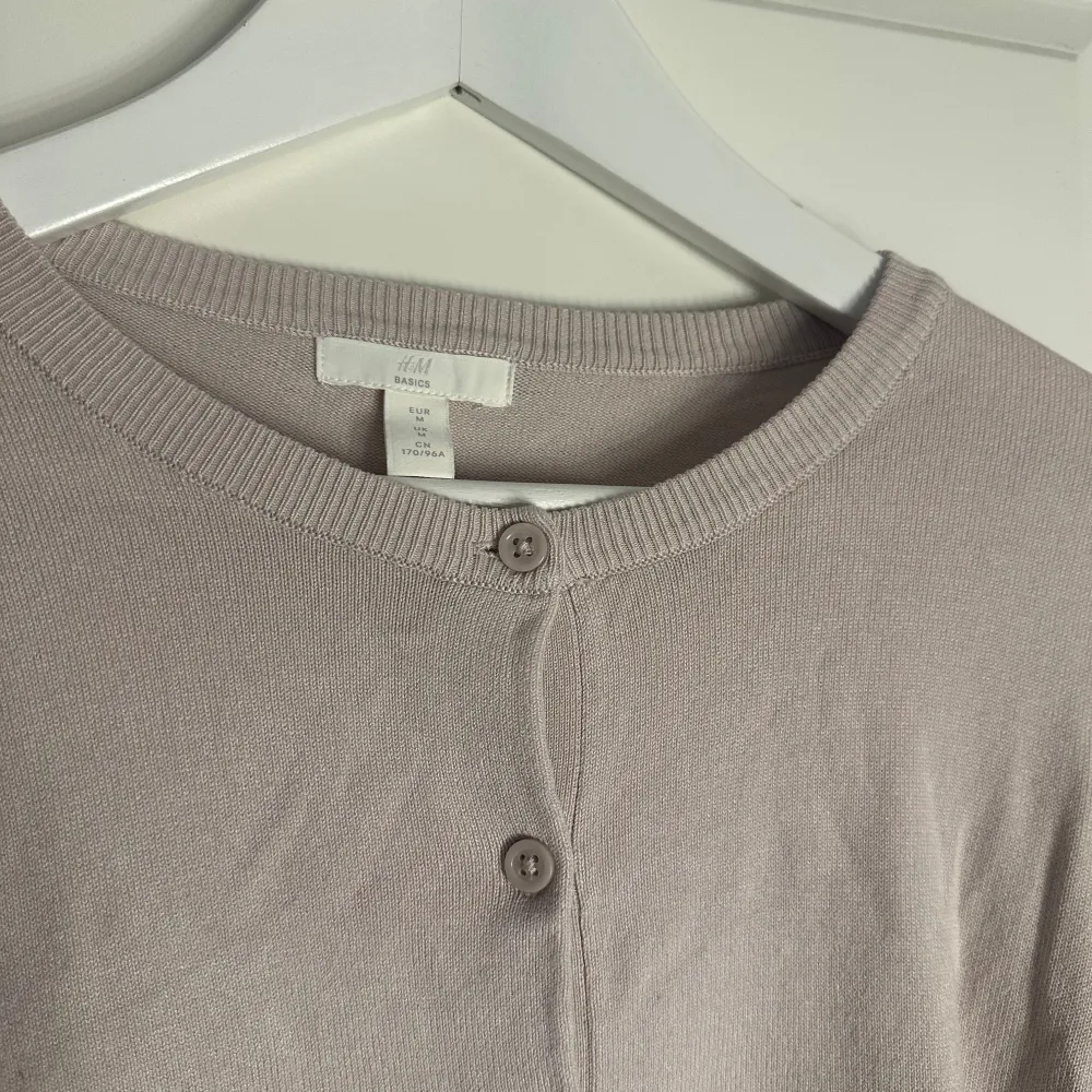 Säljer en stilren beige/rosa kofta från H&M i storlek S. Koftan har långa ärmar och knappar framtill, perfekt för lager-på-lager under kyligare dagar. Enkel och klassisk design som passar till det mesta.. Neuletakit & Villapaidat.