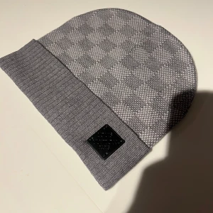 Grå stickad mössa med mönster - Snygg grå stickad mössa med diskret rutigt mönster och en ribbad kant. Perfekt för kyliga dagar.