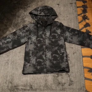 Trapstar windbreaker - svart och grå mönstrad jacka från Trapstar. Jackan har en huva och tryckknappar framtill. Perfekt för en streetwear-look. Jackan är äkta och har kvitto. Finns en liten skada som knappt syns. Storlek Xs passar S.