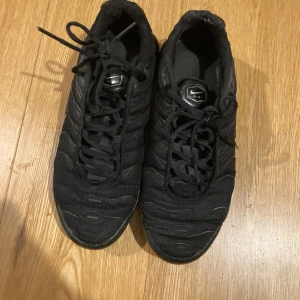 Svarta TN Nike sneakers - Säljer ett par svarta TN Nike sneakers med snörning. Skorna har en sportig design och är perfekta för vardagsbruk. De är tillverkade i syntetmaterial och har en bekväm passform.