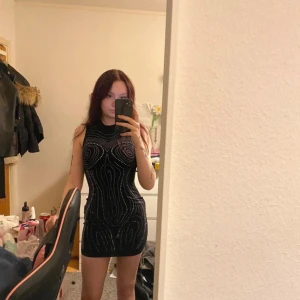 Svart glittrig klänning - Snygg svart klänning med glittriga detaljer som ger en festlig look. Den är ärmlös och har en tight passform som framhäver figuren. Perfekt för en utekväll eller festlig tillställning. Helt ny 