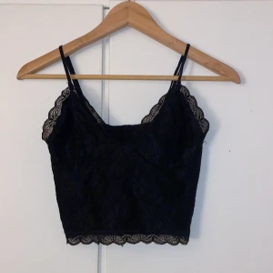 Svart spetslinne från Bik Bok - Snyggt svart spetslinne från Bik Bok i storlek XS. Linnet har smala axelband och vacker spetsdetalj längs kanterna. Perfekt för en stilren look.