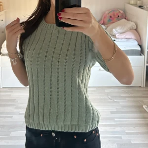 Grön stickad t-shirt - Säljer en snygg grön stickad tröja från KappAhl. Tröjan har korta ärmar och ett ribbat mönster som ger en stilren look. Den har en fin ljusgrön färg som passar bra till våren och hösten! Bara använd en gång!☺️