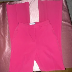 Rosa vida kostymbyxor  - Snygga rosa byxor / kostymbyxor från ASOS med hög midja och vida ben. Perfekta för en trendig look med en elegant touch. Byxorna har en slitsdetalj som ger extra stilpoäng.