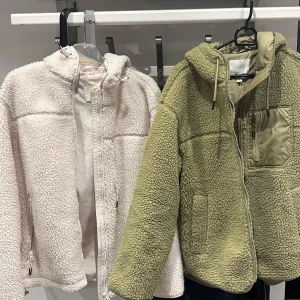 Två Teddy jackor  - Säljer två mysiga teddyjackor, en i beige och en i grön. Båda har dragkedja och huva. Den gröna och vita  jackan har en praktisk bröstficka med dragkedja. Båda två är i storlek XS. Säljer 200kr per st