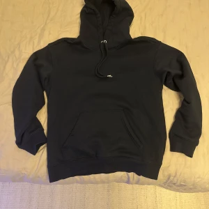 Marinblå hoodie med ficka - Säljer en klassisk marinblå hoodie med ficka och justerbar huva. Perfekt för en avslappnad stil.