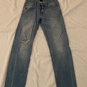 Blå jeans från Tiger Of Sweden - Snygga blå jeans från Tiger Of Sweden med slitna detaljer och en klassisk femficksdesign. De har en knappgylf och är i en ljus tvätt som ger en avslappnad look.
