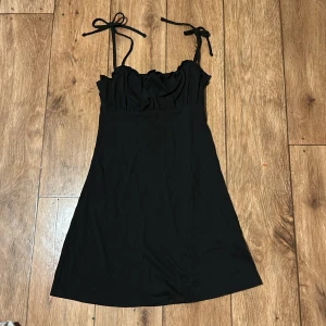 Svart klänning från Divided - Snygg svart klänning från Divided med smala axelband som knyts. Klänningen har en enkel och stilren design med en lätt rynkad överdel. Perfekt för en kväll ute eller en avslappnad dag.