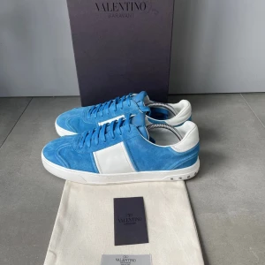 Valentino flycrew - Snygga blå och vita sneakers från Valentino Garavani. Skorna har en stilren design med snörning och är tillverkade i mocka och skinn. Perfekta för att ge din outfit en lyxig touch.