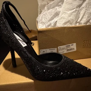 Svarta glittriga pumps från Steve Madden - Säljer ett par eleganta svarta pumps från Steve Madden. Skorna har en spetsig tå och är dekorerade med glittriga detaljer som ger en lyxig känsla. Perfekta för speciella tillfällen. Helt oanvända kommer i original skokartong. Original pris 1699kr 