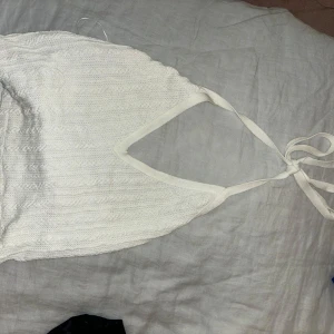 Vit stickad halterneck topp från Zara - Säljer en vit stickad halterneck topp från Zara. Toppen har en ribbad struktur och knytband i nacken. Perfekt för varma dagar eller som ett lager under en jacka.