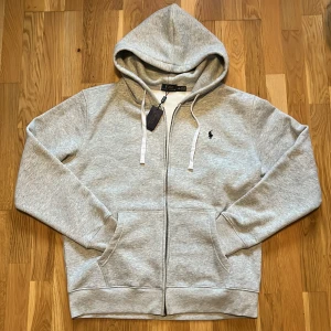 Grå hoodie från Polo Ralph Lauren - Säljer en helt ny aldrig använd polo hoodie. Tröjan är i storlek XL passar 183-190cm. Priset är ej hugget i sten! Skriv vid funderingar:)