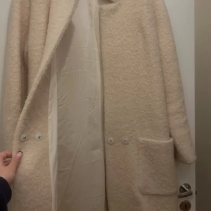 Beige kappa från Ganni - Säljer en stilren beige kappa från Ganni i storlek M. Den har en enkel design med knappar framtill och stora fickor. Perfekt för höst och vår. Andvänd 2 gånger, pris kan diskuteras vid SNABB affär 