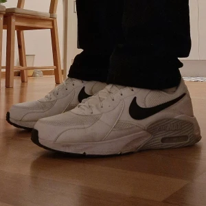 Vita Nike Air Max Excee Sneakers - Säljer ett par vita Nike Air Max sneakers med svart swoosh. Skorna har en klassisk design med snörning och synlig luftdämpning i sulan för extra komfort. Nypris: 1350 hos Nike. Använda ett tag men ser helt nya ut efter en tvätt. 