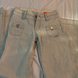 Ljusblåa jeans från Roxy - Snygga beige flare jeans från Roxy med flätade bälteshällor och dekorativa knappar på fickorna. Helt nya