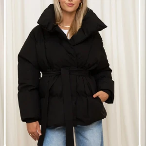 Svart pufferjacka från GetMod - Snygg svart pufferjacka från GetMod med bälte i midjan för en definierad siluett. Jackan har långa ärmar och en hög krage som skyddar mot kyla. Perfekt för kalla dagar när du vill hålla stilen. Jag köpte den för 1 149kr från Nuvelle och jag har inte använt den pga den är för stor på mig och det går inte att lämna tillbaka!