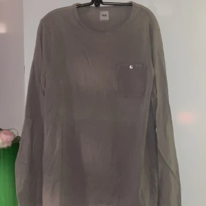 Grå långärmad tröja från ASOS - Säljer en stilren grå långärmad tröja från ASOS. Tröjan har en bröstficka med knappdetalj som ger en extra touch. Perfekt för en avslappnad look.