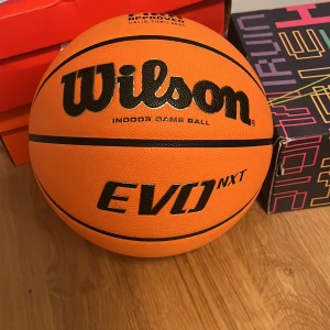 Basketboll Wilson EVO NXT - Säljer en Wilson EVO NXT basketboll, perfekt för inomhusspel. Bollen är FIBA-godkänd och har en orange färg med svarta detaljer. Den är designad för att ge bra grepp och kontroll under spelet. Passar utmärkt för både träning och match. En av de nyare modellerna som släpptes 2023. Bara använd ett fåtal gånger och i mycket bra skick. Ny pris 1000