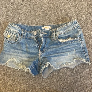 Blå jeansshorts med fransar - Snygga blå jeansshorts från Gina Tricot med fransiga kanter och klassiska femficksdesign. Perfekta för sommardagar och festivaler. De har en knapp och dragkedja framtill samt dekorativa sömmar. Dom är i storlek 152 men passar mig som är 165.