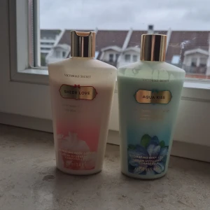 Body lotions från Victoria's Secret - Två body lotions från Victoria's Secret: 'Sheer Love' i en ljusrosa flaska och 'Aqua Kiss' i en ljusblå flaska. Båda har guldiga lock och är designade för att återfukta huden med en lätt doft.
