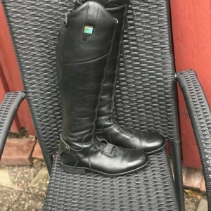 Svarta ridstövlar Bocaj 37-38 - Snygga svarta ridstövlar med dragkedja på baksidan. Perfekta för ridning och ger ett stilrent intryck. liten klack och rundad tå. Bredd 35 cm och höjd 45 cm från klacken. Storlek 37 men passar mig som har 38. De är välanvända men fortfarande fina