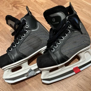 Svarta och grå skridskor från Revolution stl 37 - Säljer ett par svarta och grå skridskor från Revolution, modell T2. De har snörning och en robust design med syntetmaterial. Stl 37