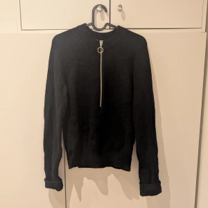 Svart stickad tröja från NA-KD - Säljer en stilren svart stickad tröja från NA-KD med en snygg dragkedja framtill. Tröjan har långa ärmar och en ribbad struktur som ger en skön passform. Perfekt för kyligare dagar! Lite nopprig men fortfarande fin!