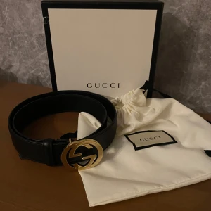Svart skärp från Gucci - Snyggt svart skärp från Gucci med en ikonisk dubbel G-spänne i guld. Tillverkat i skinn och kommer med originalförpackning och dustbag. Perfekt för att ge en lyxig touch till din outfit.