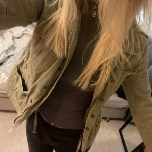 Olivgrön jacka - Säljer en snygg olivgrön jacka. Den har coola nitar på kragen och praktiska fickor framtill. Perfekt för höst och vår! Jackan har en dragkedja och knappar för extra stil och funktionalitet. Passar perfekt för en casual look. Står storlek s men skulle säga ett den är s/xs