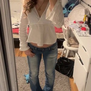 Low waist jeans - Säljer en superfin vit omlottopp med långa ärmar och volangdetalj i nederkant. Perfekt för både vardag och fest! Toppen har en v-ringad design som ger en snygg och stilren look. Passar perfekt till jeans eller kjol. Hör av dig vid intresse! 🤍