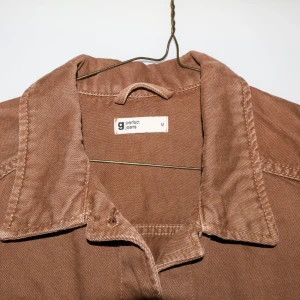 Brun croppad jeansjacka från Gina Tricot - Säljer en snygg brun croppad jacka från Gina Tricot. Jackan har en klassisk krage och knappar framtill. Perfekt för höst och vår!