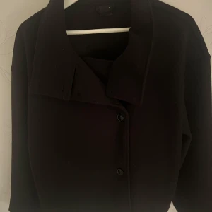 Svart kappa med knappar - Säljer en stilren svart kort kappa i nyskick från Gina Tricot. Storlek M. Aldrig använd. 