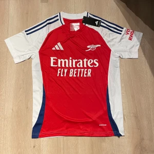 Arsenal fotbollströja  - Säljer en replika av Arsenals hemmatröja 24/25, storlek S. Tröjan är i perfekt skick, aldrig använd och har alla originaltaggar kvar. 
