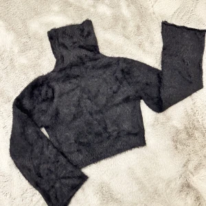 Svart fluffig polotröja - Supermysig svart fluffig polotröja som är perfekt för kyliga dagar. Den är croppad och har långa ärmar, vilket gör den både trendig och bekväm. Perfekt för att hålla sig varm och stilren samtidigt!