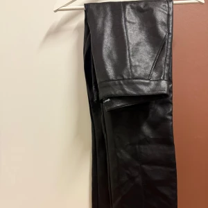 Oanvända Svarta skinnbyxor från Gina Tricot - Säljer ett par snygga svarta skinnbyxor i mycket bra skick. De är högmidjade och har en straight passform. Passar både till vardags och fest! De är helt oanvända. Jag hade köpt dem för ~600kr🤎