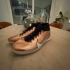 Säljer ett par grymma Nike fotbollsskor i en cool kopparfärg med svarta detaljer och snörning. Skorna har en hög krage för extra stöd för de är ACEDEMY och en vit sula. Perfekta för inomhusfotboll eller konstgräs. De är i mycket bra skick. Lite defekter men inget som stör spelet