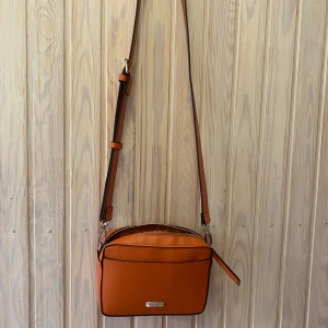 Orange axelväska från Don Donna - Säljer en snygg orange axelväska från Don Donna i mycket bra skick. Väskan har en justerbar axelrem och en praktisk dragkedja upptill. Perfekt för både vardag och fest! 🧡